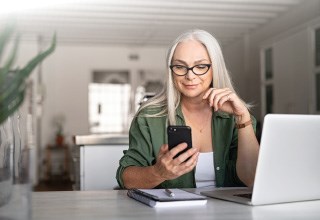 woman with a laptop and notebook is looking at her cell phone