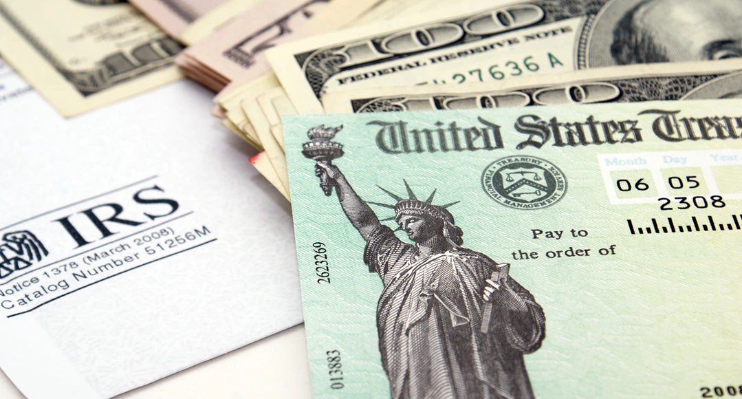 IRS envelope and tax refund check spread on a table with U.S. $100 and $50 bills.