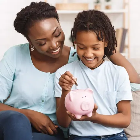 mom and daughter put a coin in a piggy bank on a couch