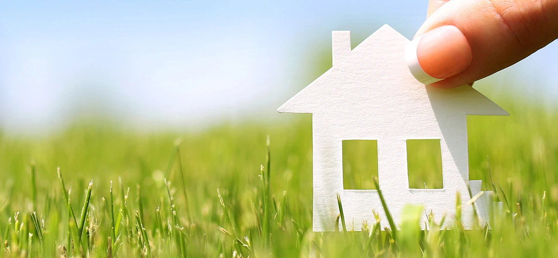 Person placing a cutout of a home in an open field.